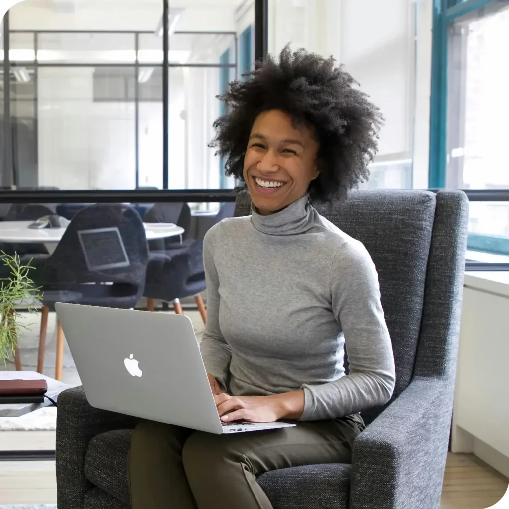 A woman sitting in a chair smiling while using a laptop.