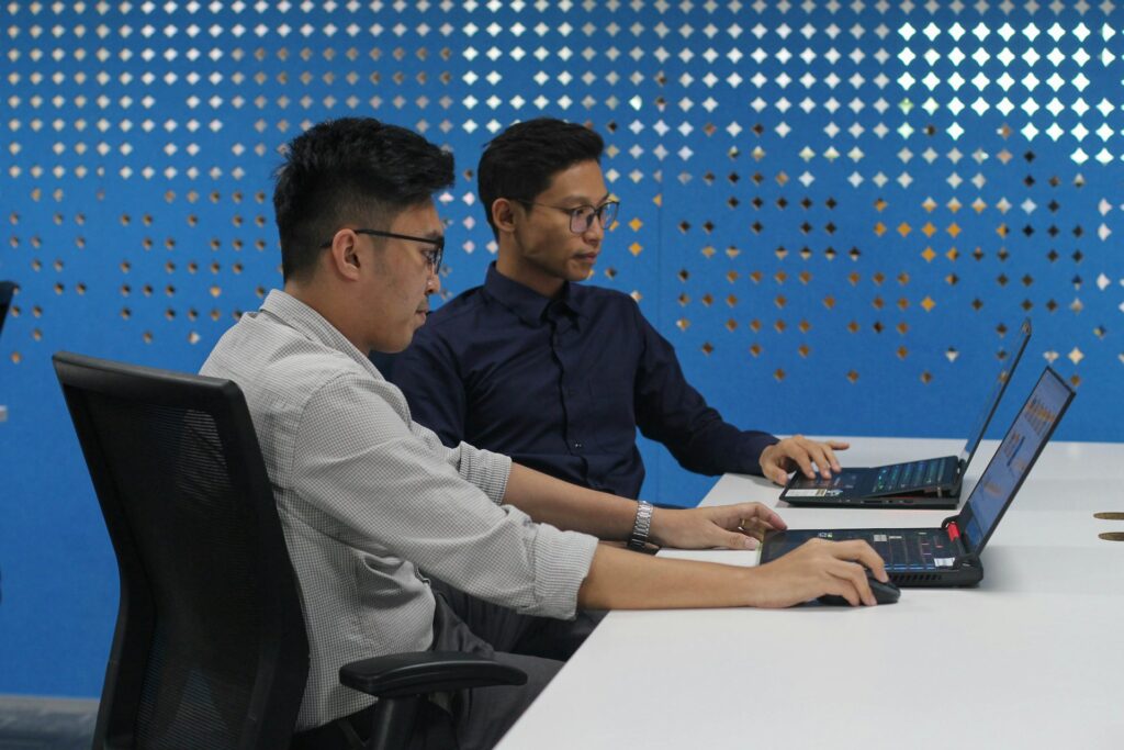 two people working at a desk with laptops