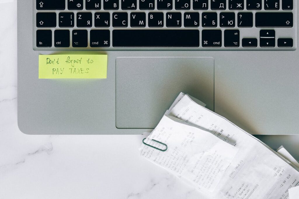 Macbook with Receipts and a Sticky-Note Saying “Don’t Forget to Pay Taxes”.