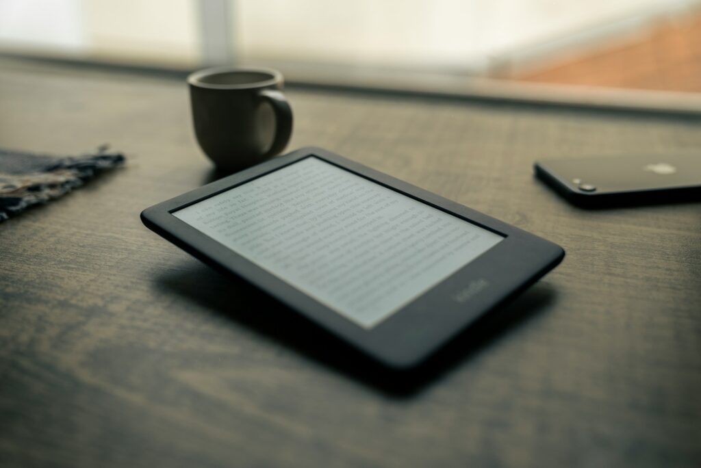 An e-reader next to a phone and a coffee cup